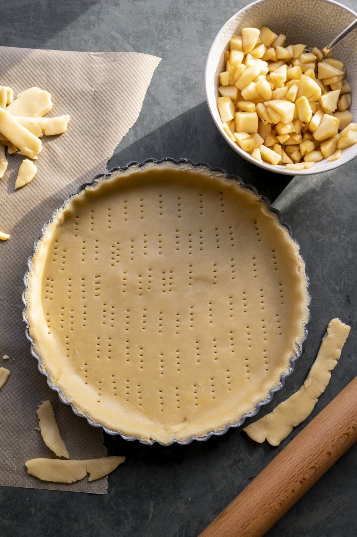 Pie crust in tin with fork holes with bowl of apple mix on the side