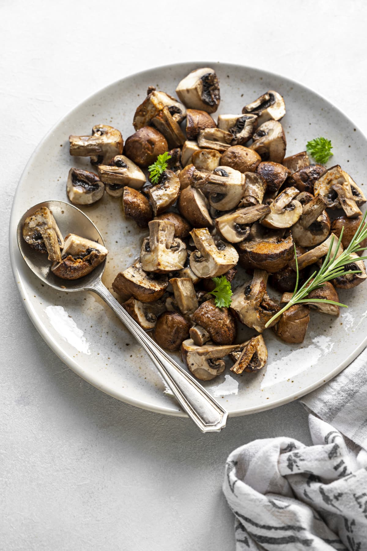 Baked mushrooms on white plate with seasonings and green garnish and silver spoon