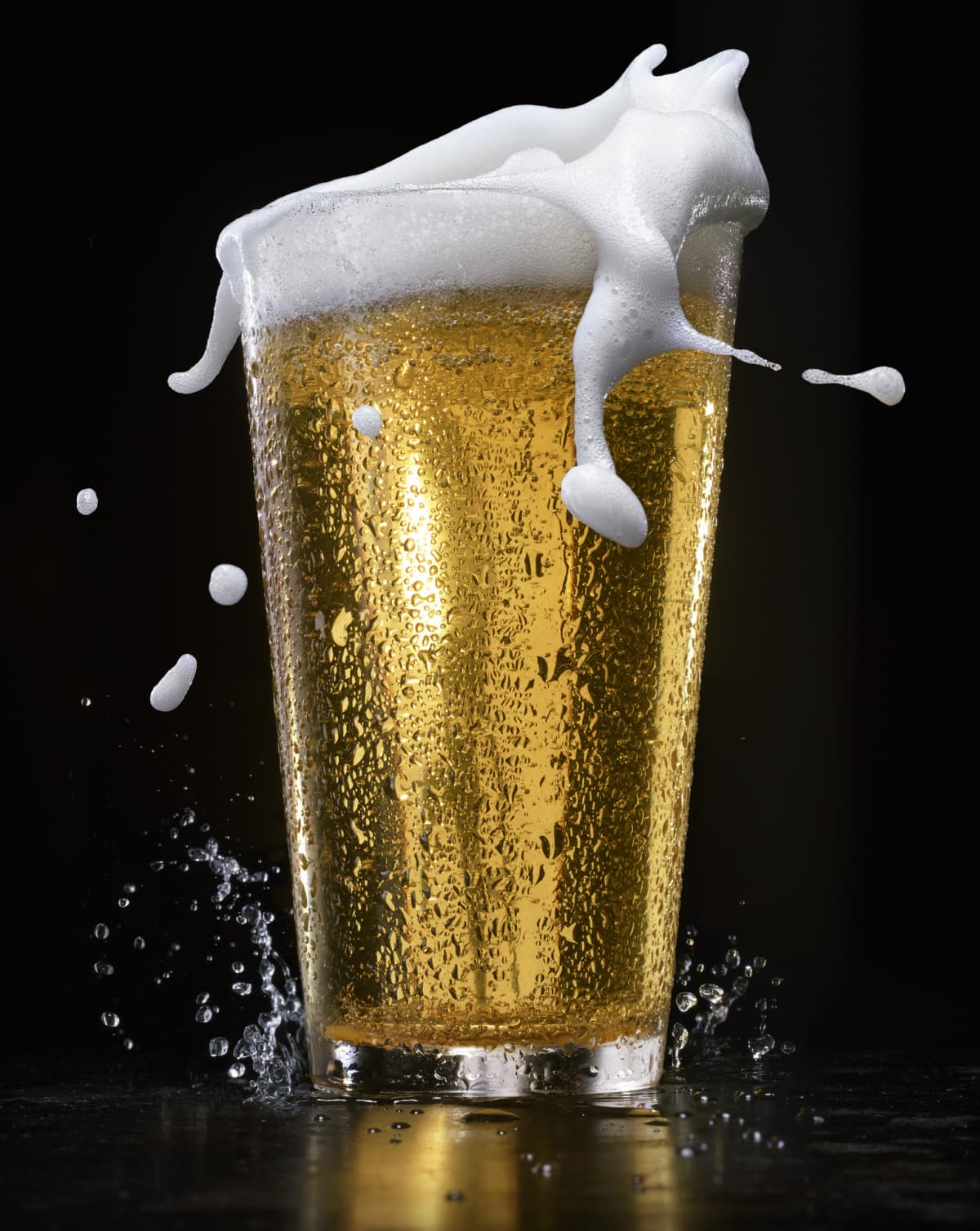 A glass of beer with foam splashing out of the top.