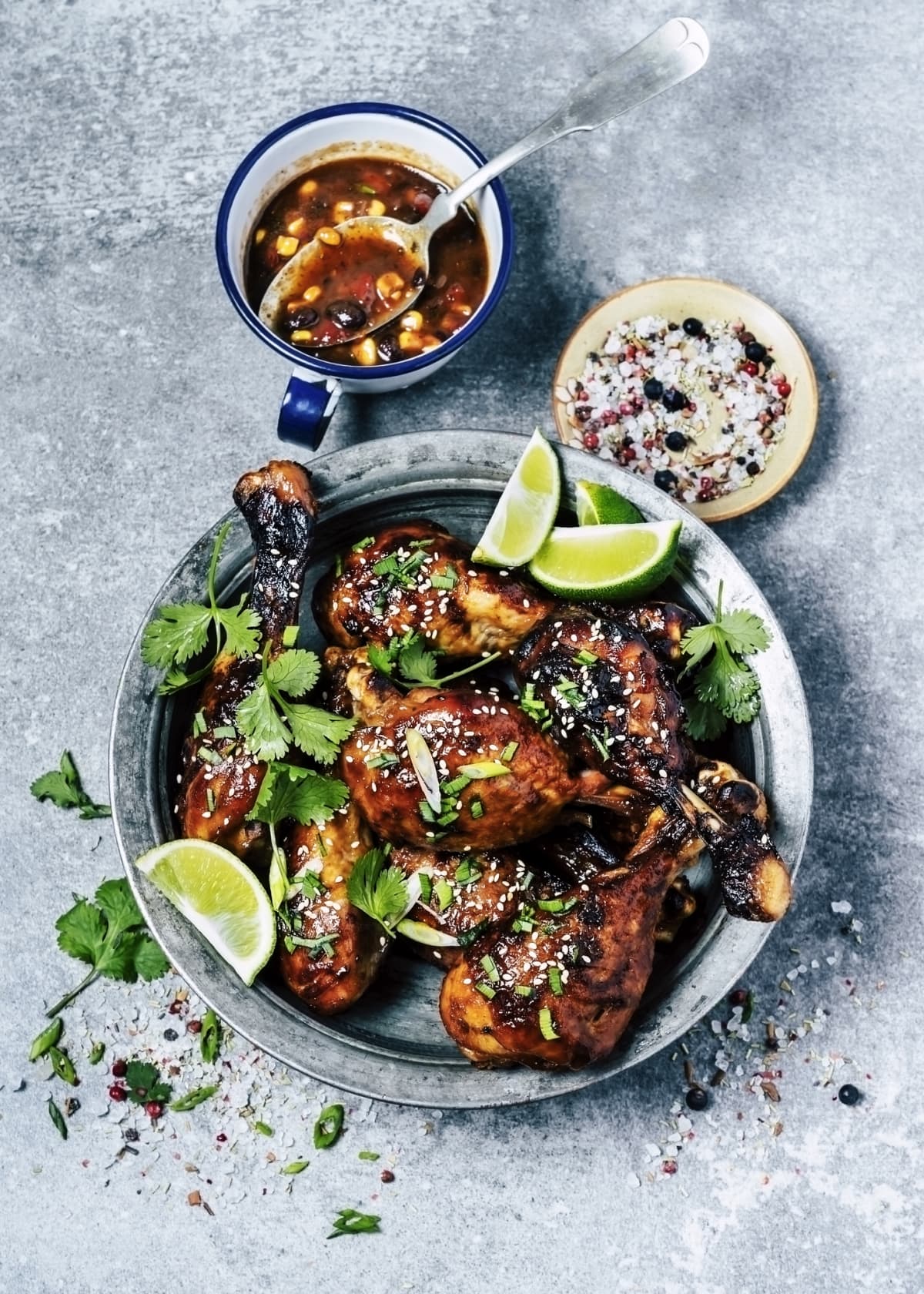 A bowl of roasted chicken legs with corn salsa and spices on gray background