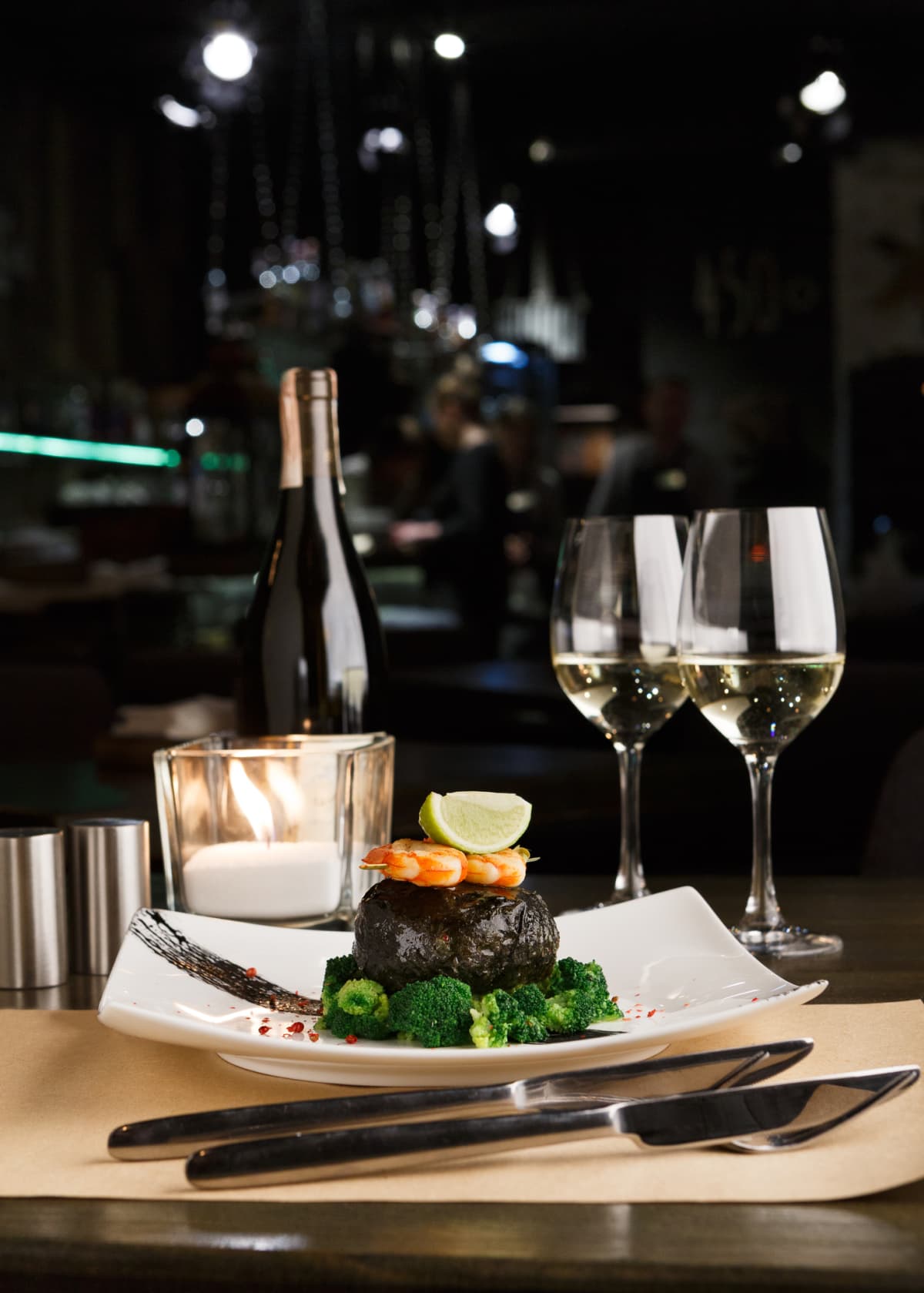 Wining and dining at restaurant. Dorado fillet wrapped in nori on steamed broccoli with shrimps and lemon piece. Table served with wine and fine cutlery for luxurious dinner. Gourmet cuisine meals
