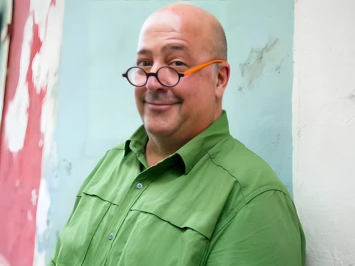 Andrew Zimmern smiling in front of a blue wall.