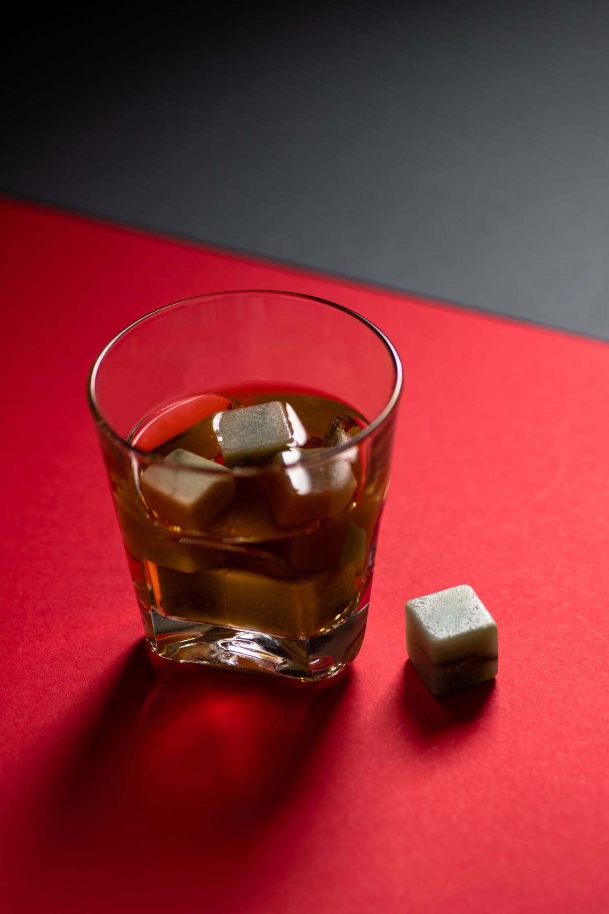 Whiskey and whiskey stones in a glass on a red and black background. Minimalistic composition. Copy space