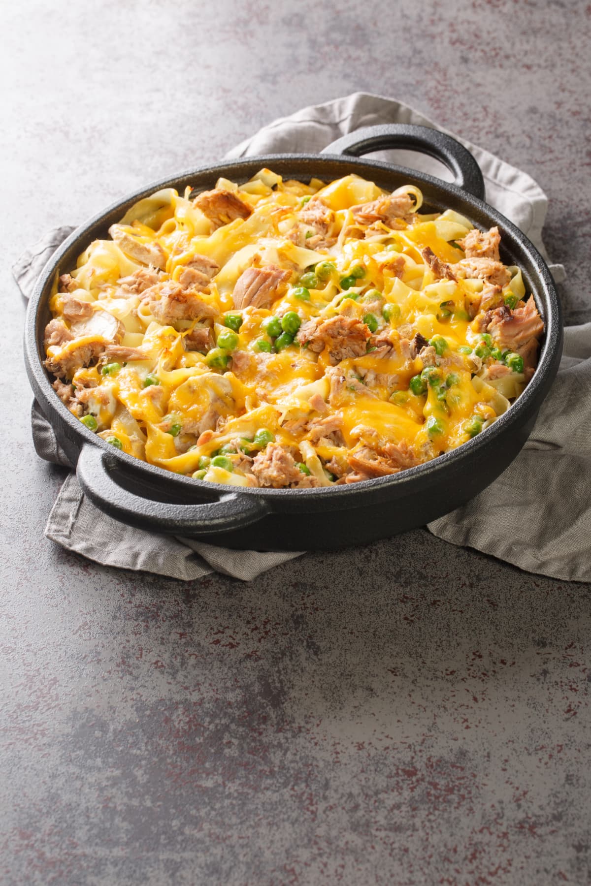 Canned Tuna casserole with pasta, green peas, mushrooms and cheddar cheese close-up in a baking dish on the table. Vertical