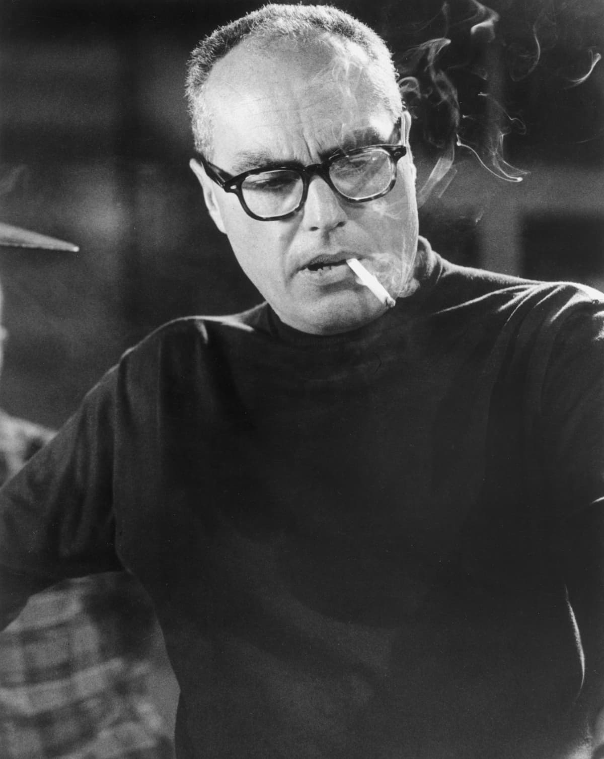 circa 1955:  Headshot of American film director John Sturges (1910 - 1992) wearing a black turtleneck and glasses with a cigarette dangling from his lips and smoke swirling up.  (Photo by Hulton Archive/Getty Images)