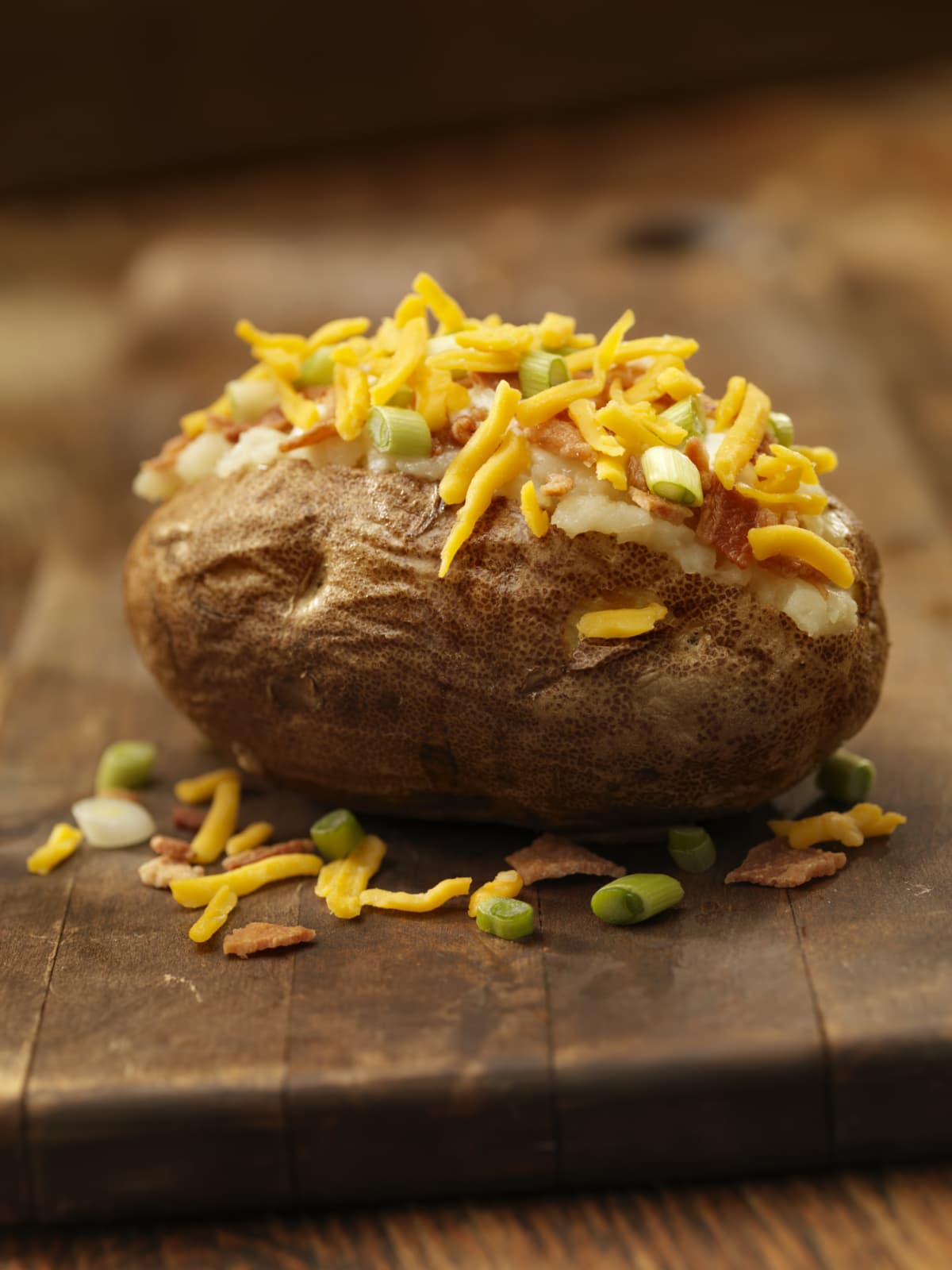 Baked potato topped with bacon, sour cream, green onions, and cheddar cheese on cutting board