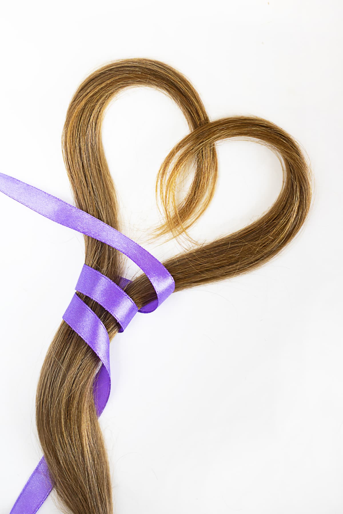 A lock of hair formed into a heart tied with a purple ribbon to symbolize hair donation for a cancer charity