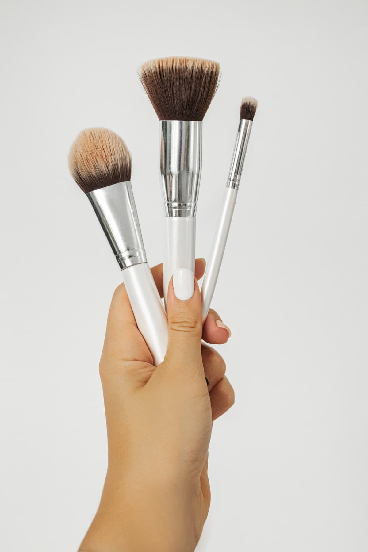 Hand holding three different types of duo-fiber makeup brushes