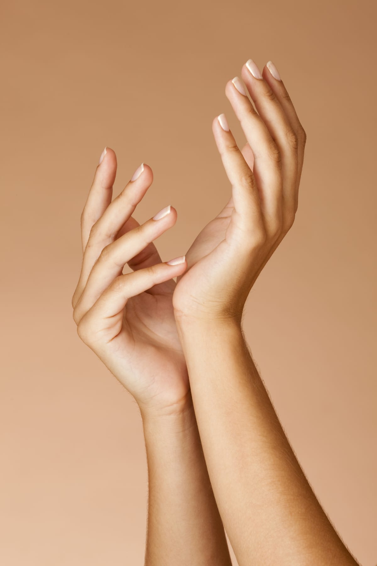 Close up of two hands with healthy nails against a tan background