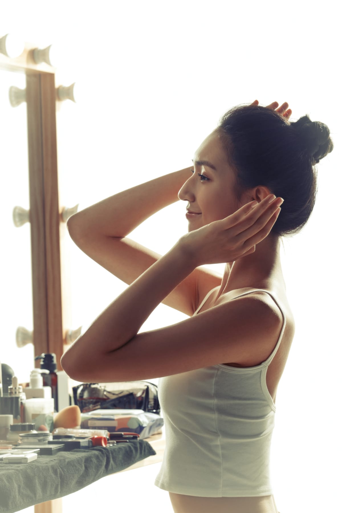 woman slicking her hair back into a high bun in the mirror