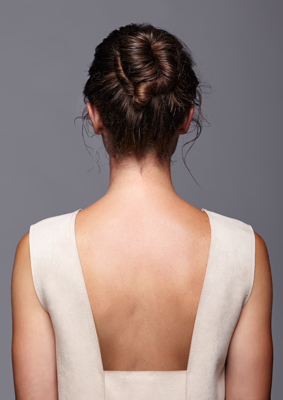 Picture of a woman from behind, her hair is in an updo and she has a blunging dress on revealing the nape of her neck