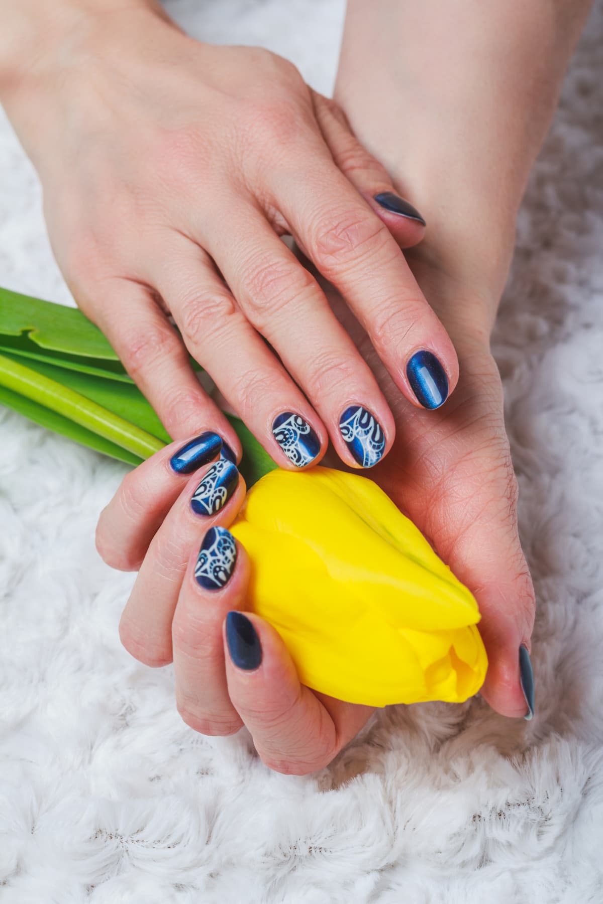 closeup of hands with a blue polish manicure with lace nail art