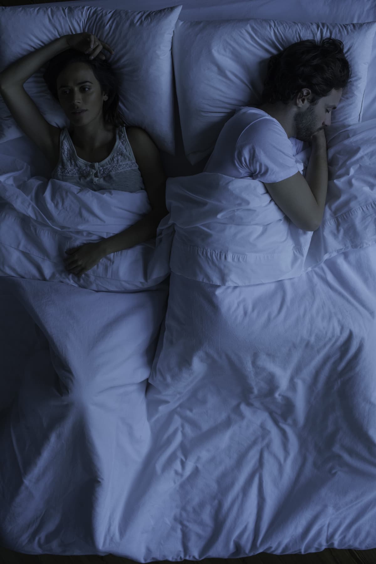 A woman lies awake in bed in the middle of the night worried that her partner who is sleeping soundly has grown distant