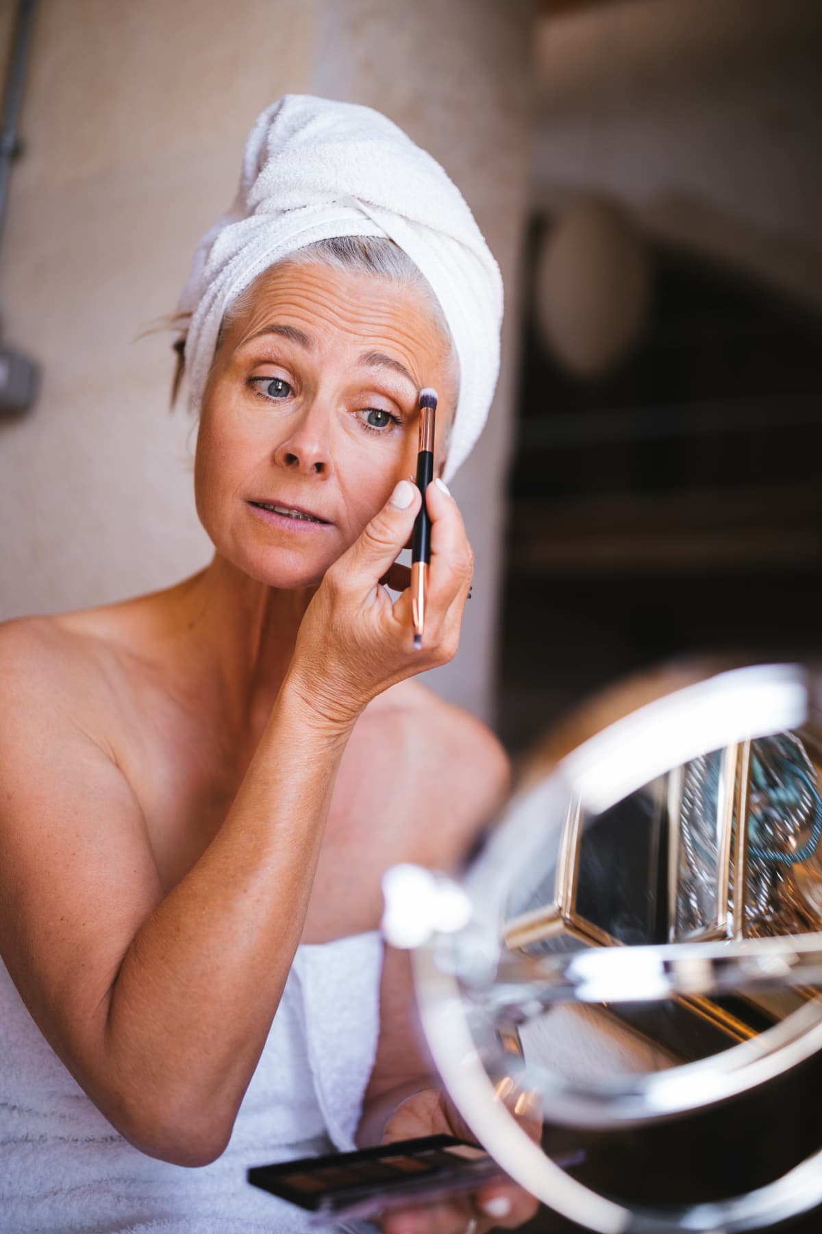 a mature woman applying bronzer to her face with a makeup brush
