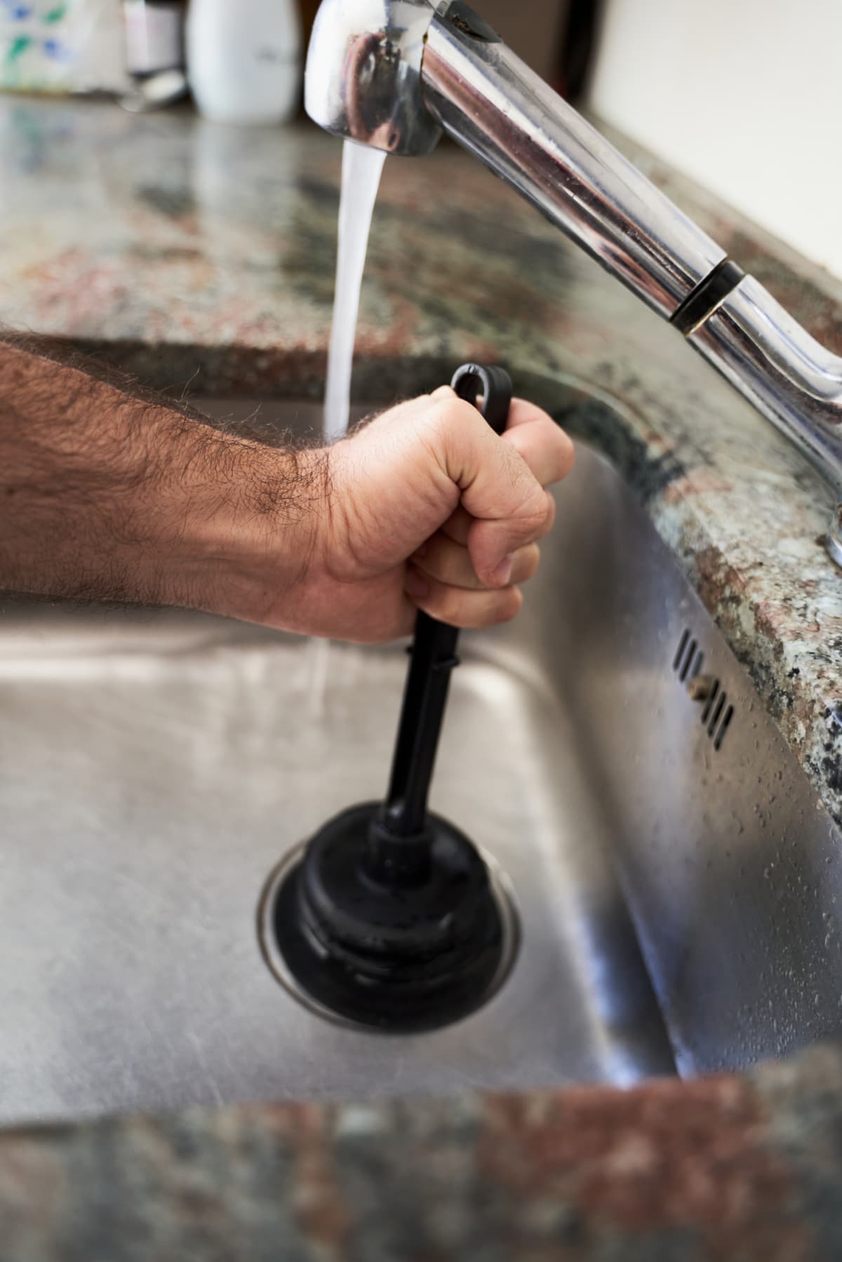 A person using a pipe plunger to clear kitchen sink