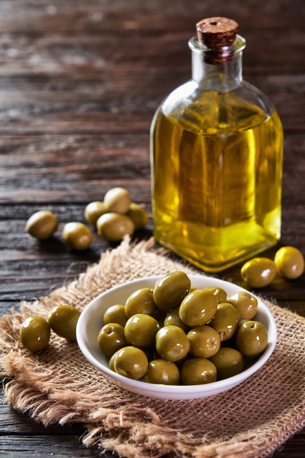 Olive oil bottle and green olives on a bowl on rustic wooden table