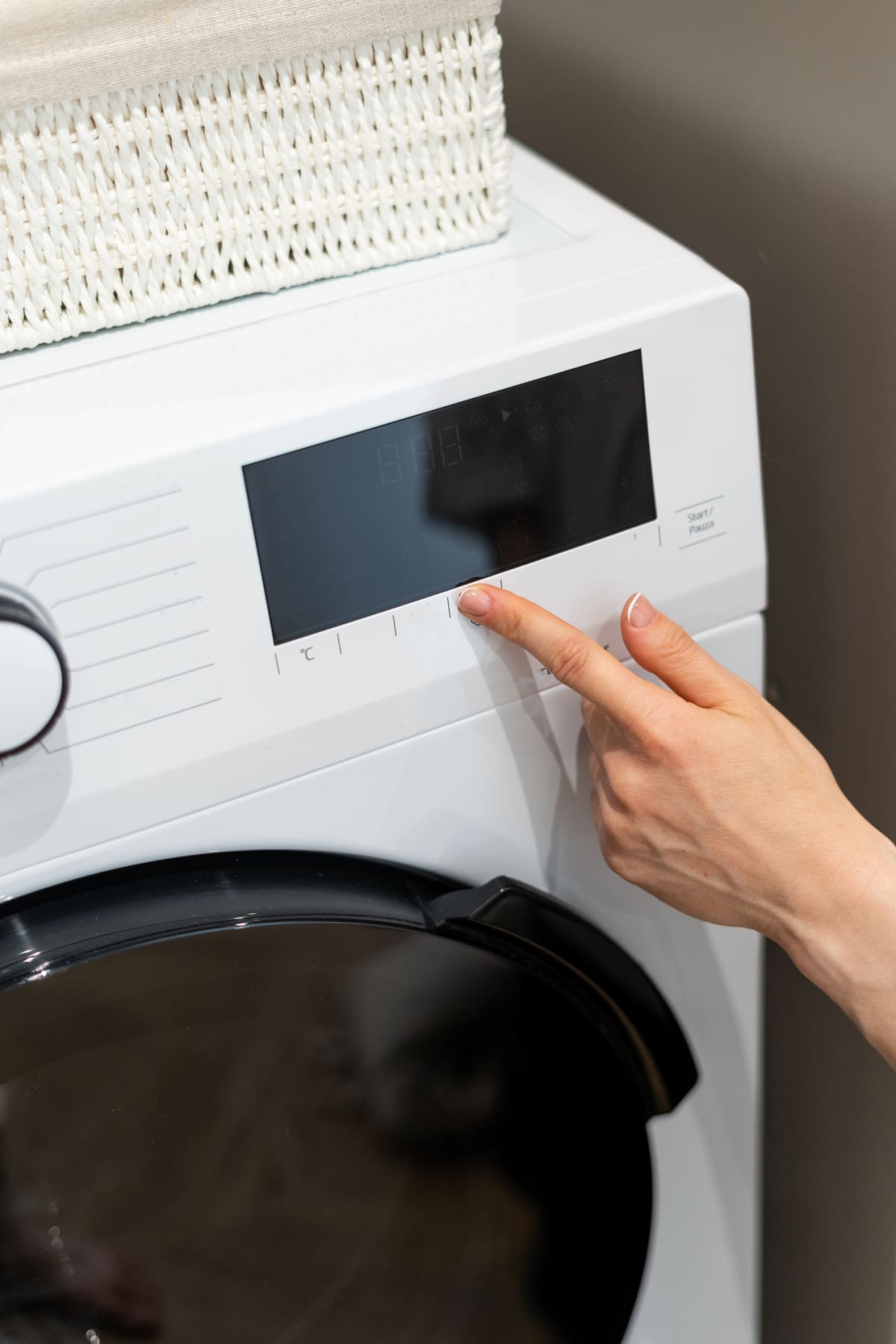 Woman's hand pressing buttons on washing machine before doing laundry