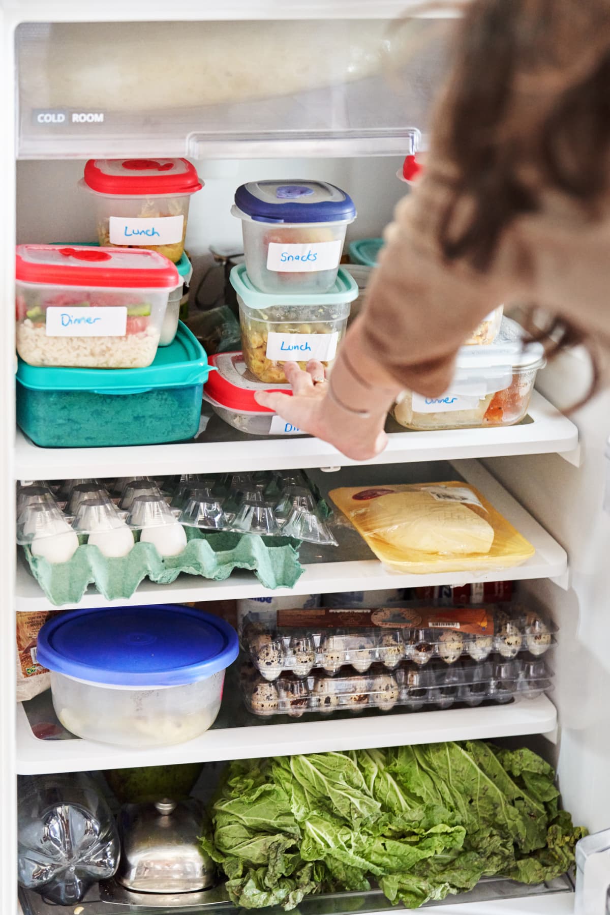 Close-up of a woman looking through containers of healthy prepared meals stacked in her refrigerator at home.