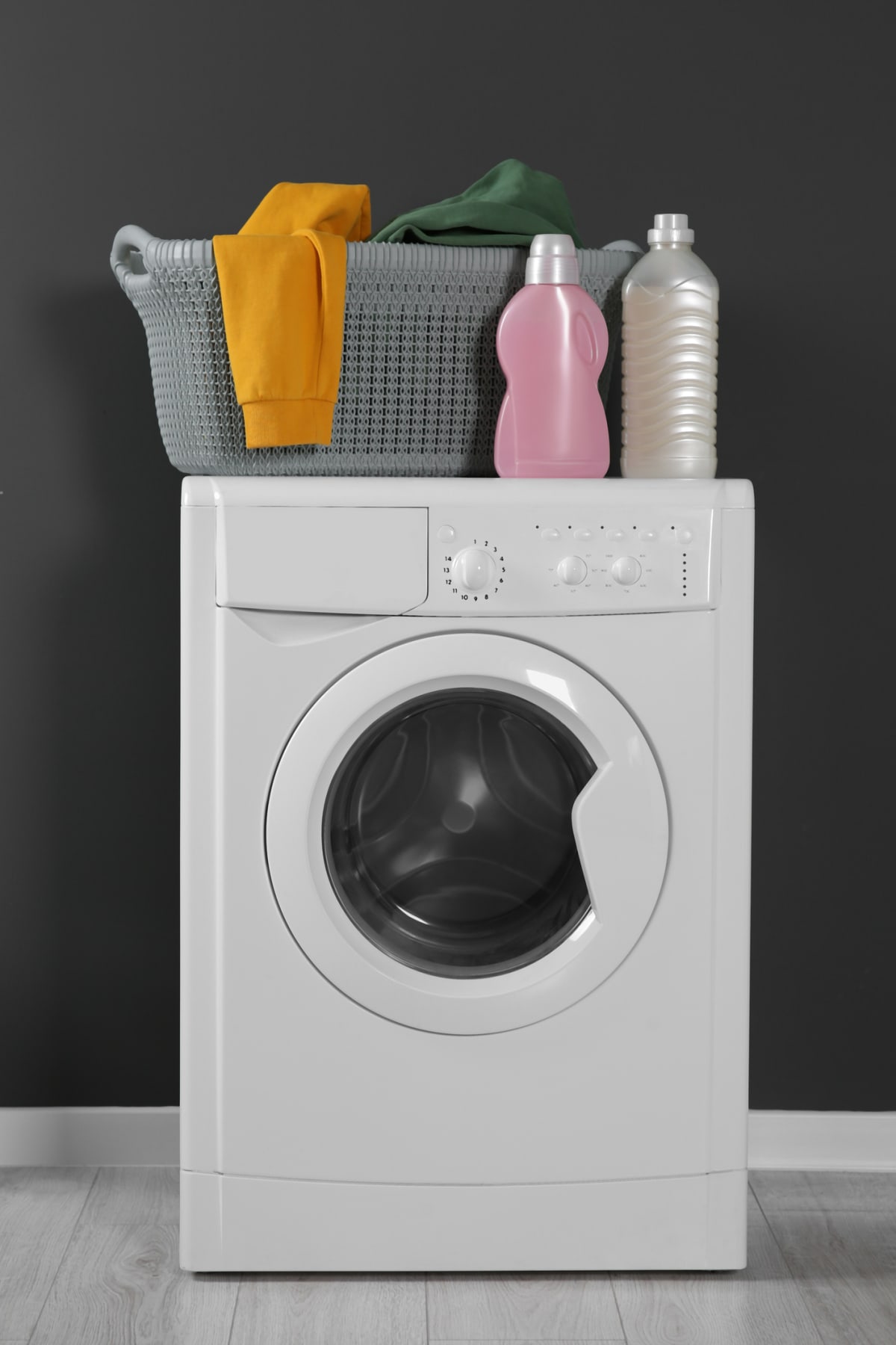 Washing machine with clothes and detergents near black wall indoors. Interior design.