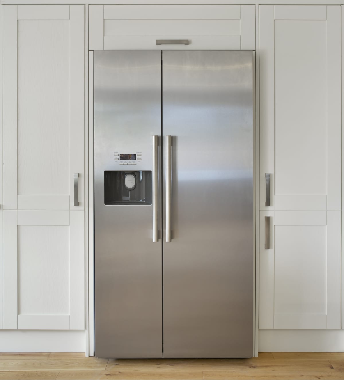 A modern American fridge freezer set into a bank of cream colored cupboards.