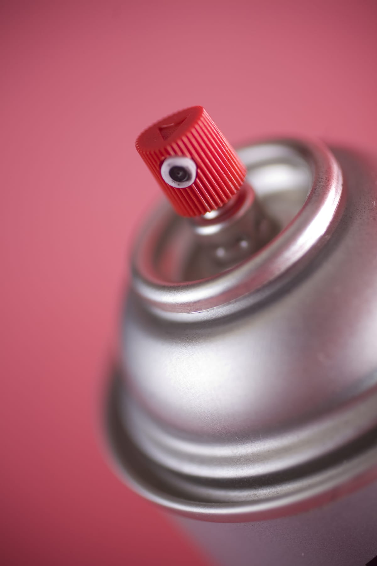 Spray paint can with a red nozzle on a colored background.