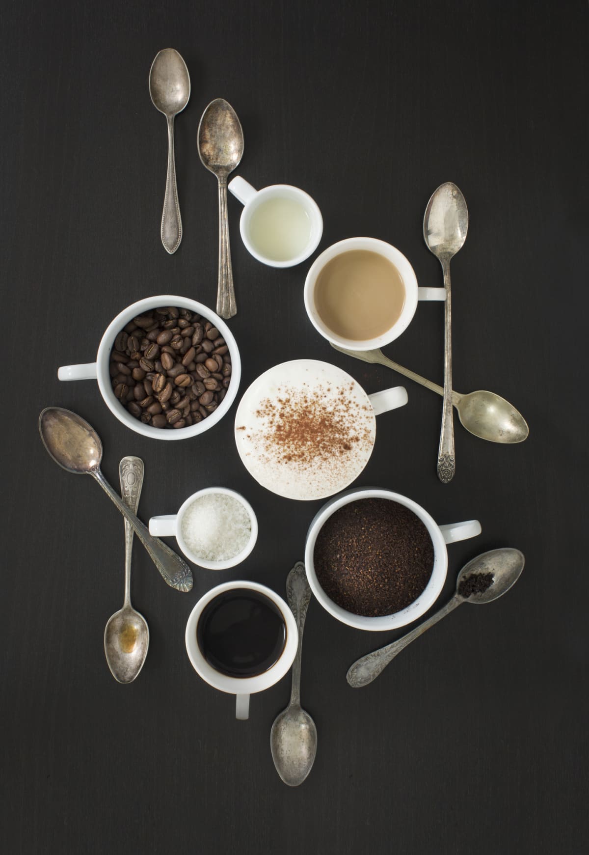 Overhead view flat lay coffee drinks ingredients on black wooden background with vintage spoons. Stylized coffee image.