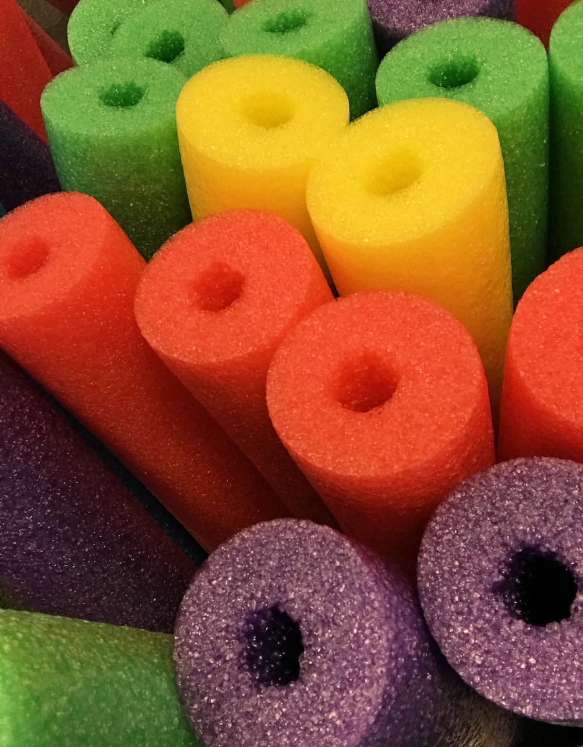 Foam pool noodles in green, yellow, orange, and purple colors