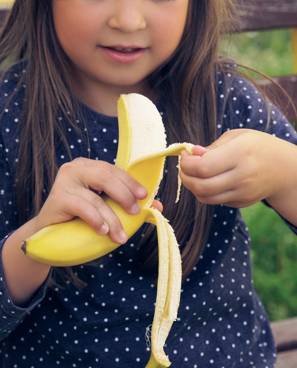 Healthy little girl eating banana. Happy kid enjoy eating fresh fruit.
