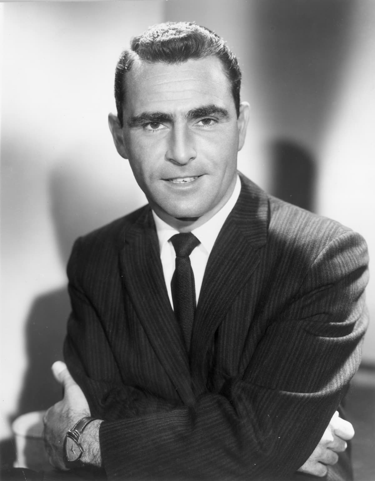 September 1963:  Studio portrait of American television writer and producer Rod Serling, the creator of the series, 'The Twilight Zone,' smiling while standing with his arms folded across his chest in a jacket and tie.  (Photo by Hulton Archive/Getty Images)