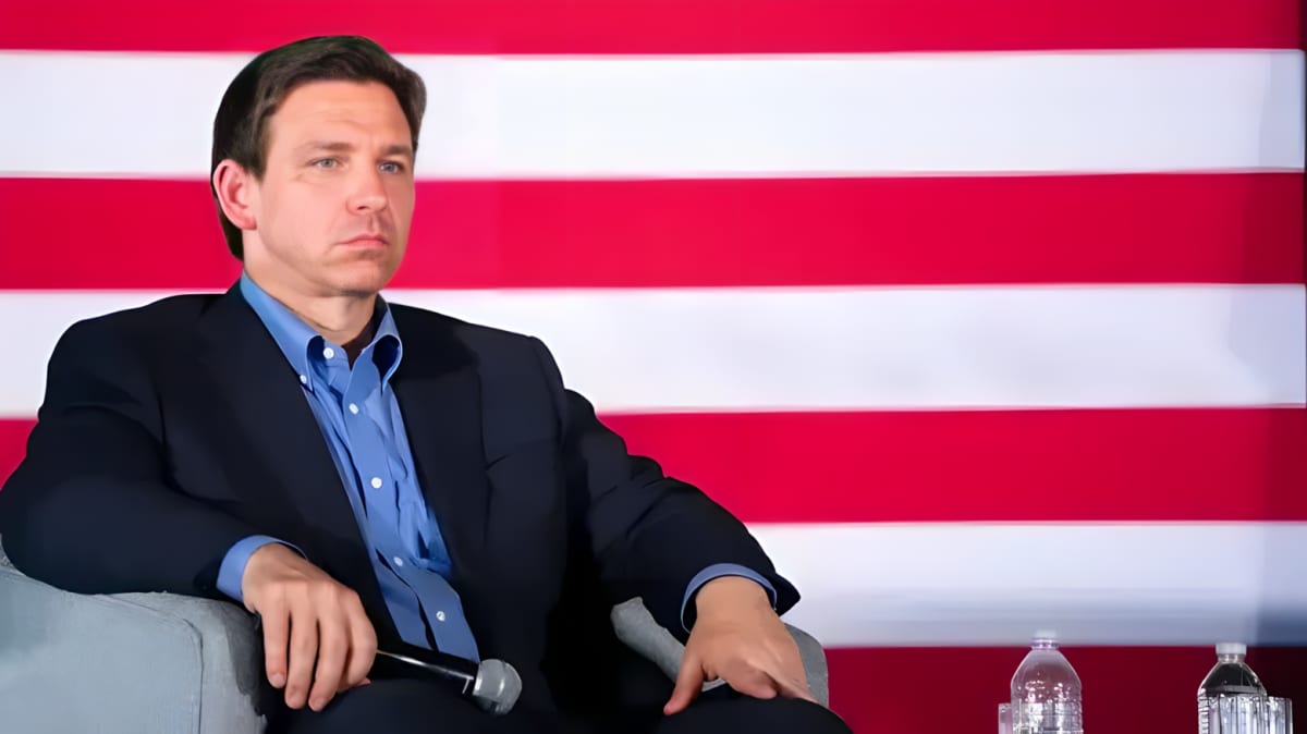 Ron DeSantis sitting and posing with mic in hand.