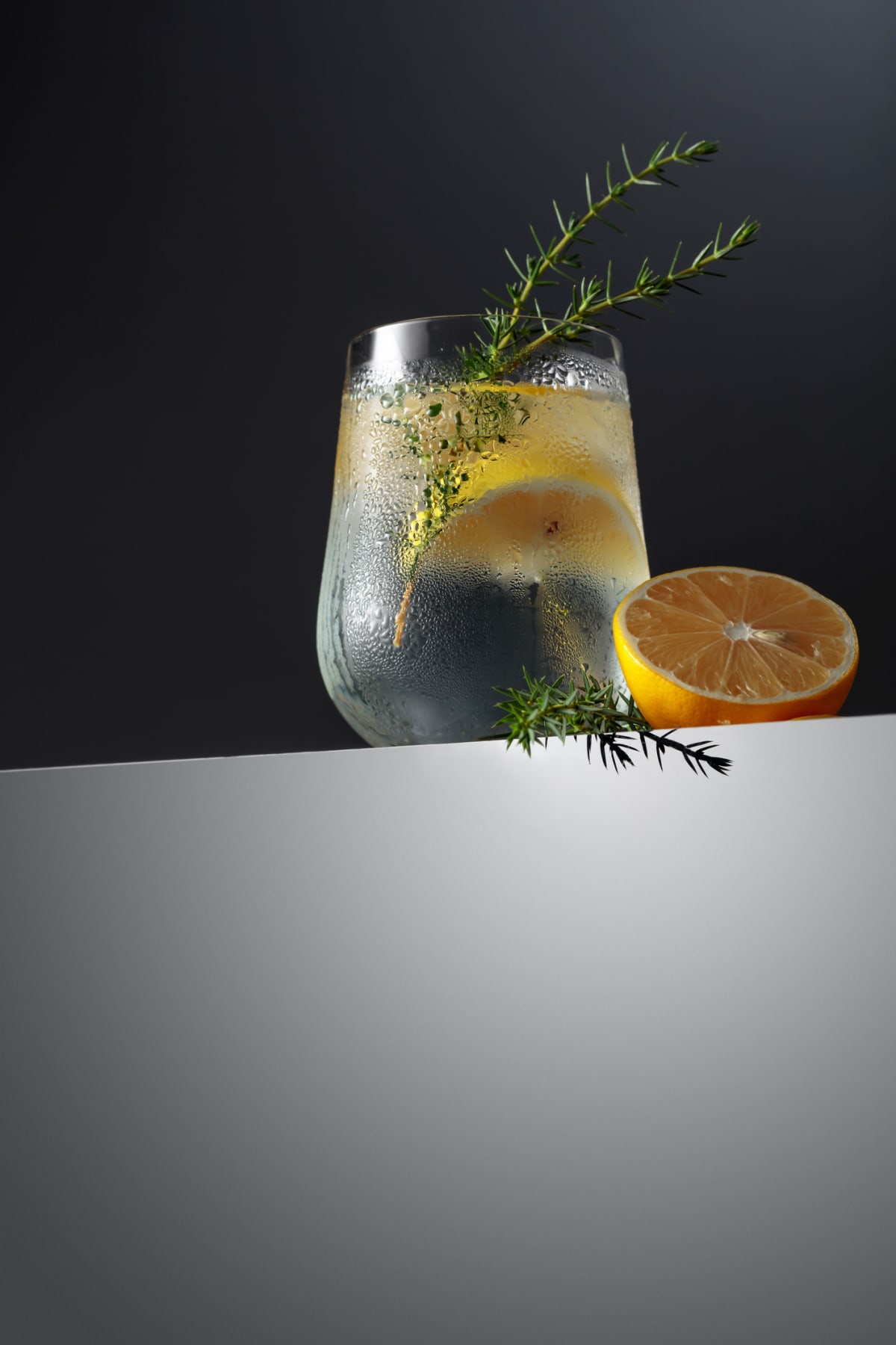 Gin and Tonic Alcohol drink with Lime, Rosemary and ice on rustic black table.