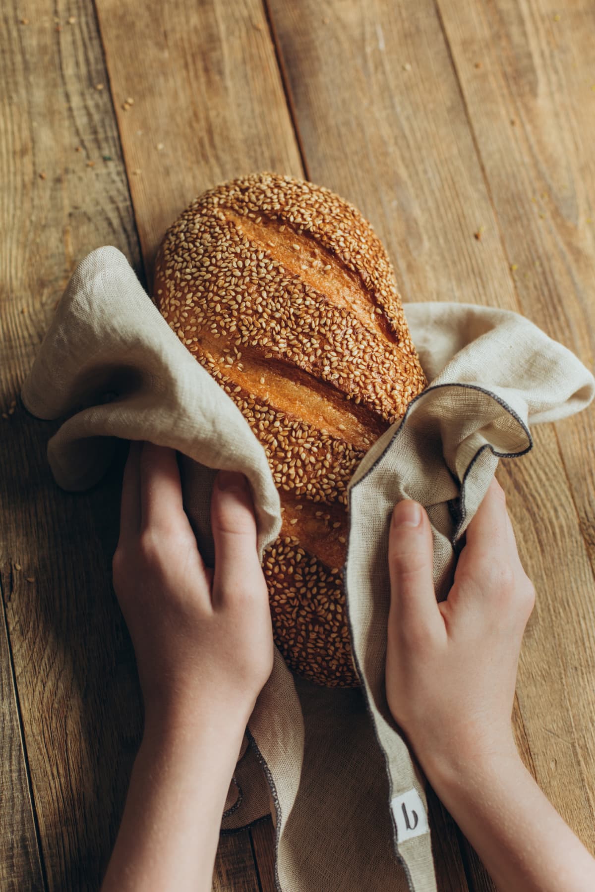 Loaf with sesame seeds, wrapped in a napkin, in children's hands on a wooden table.
