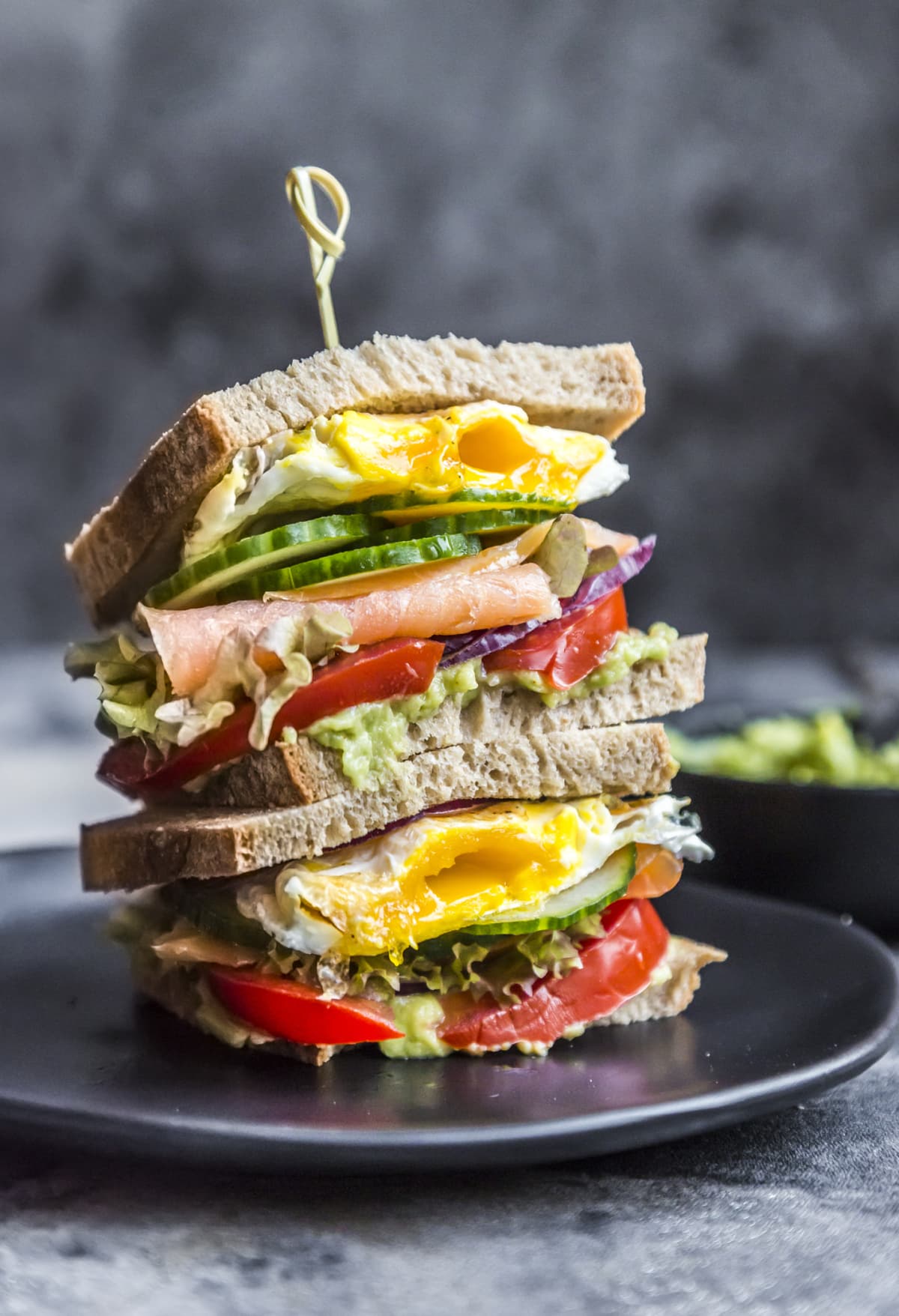 Two stacked sandwiches with tomato, egg, cucumber, and ham