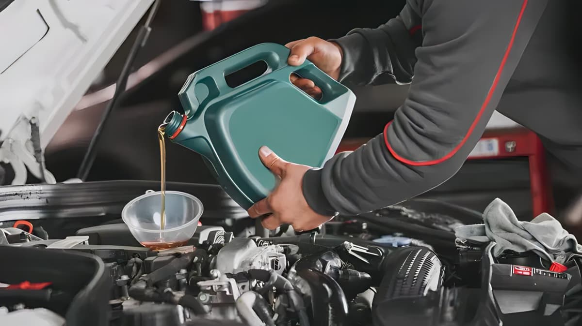 A person pouring oil into an engine from a large green bottle