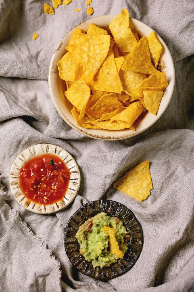 Tortilla nachos corn chips with avocado guacamole and tomato sauce served in ceramic bowl over linen folded cloth as background. Flat lay. space. (Photo by: Natasha Breen/REDA&CO/Universal Images Group via Getty Images)