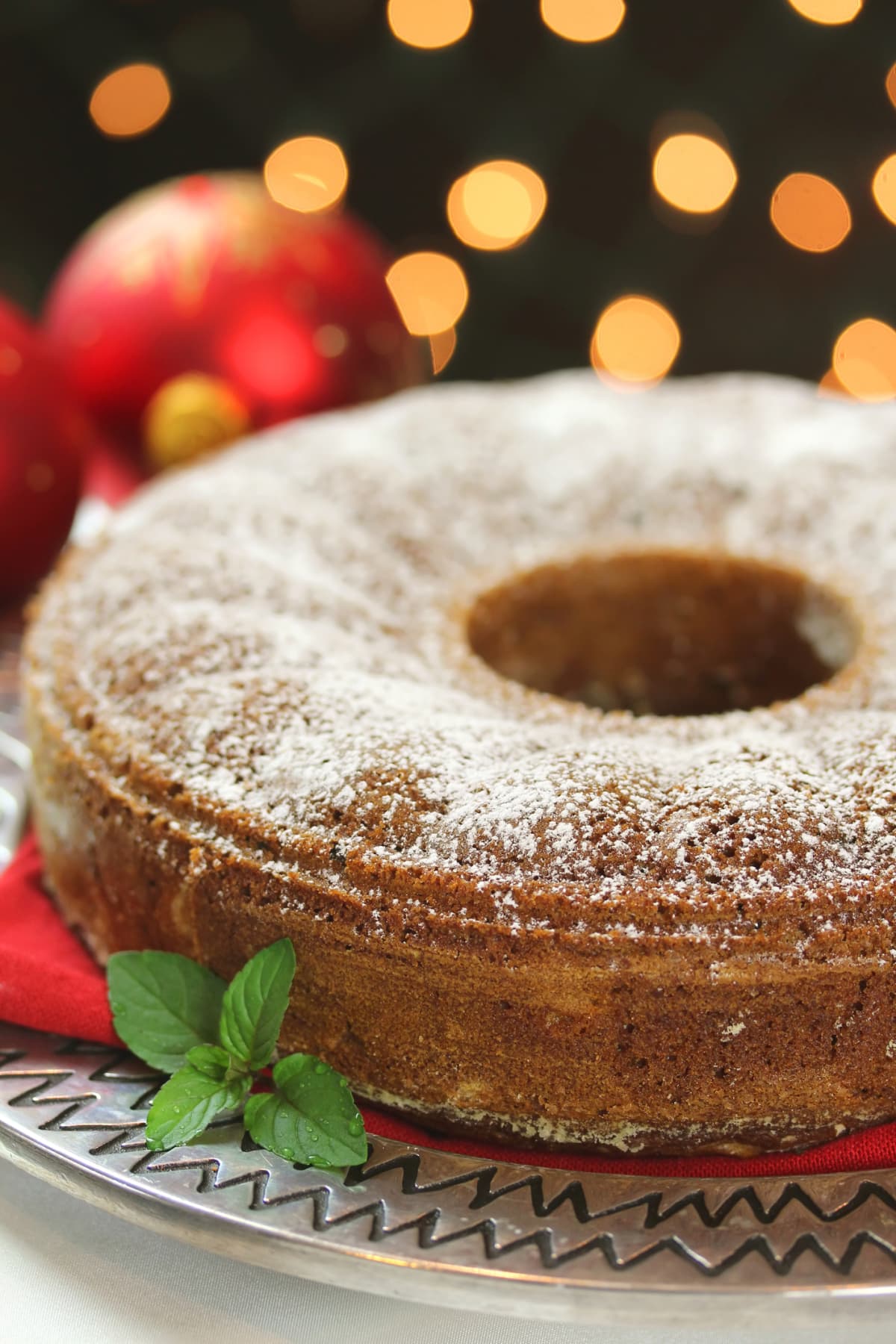 Vertical image of a dessert spice cake at Christmas time in a holiday setting with lights and ornaments.