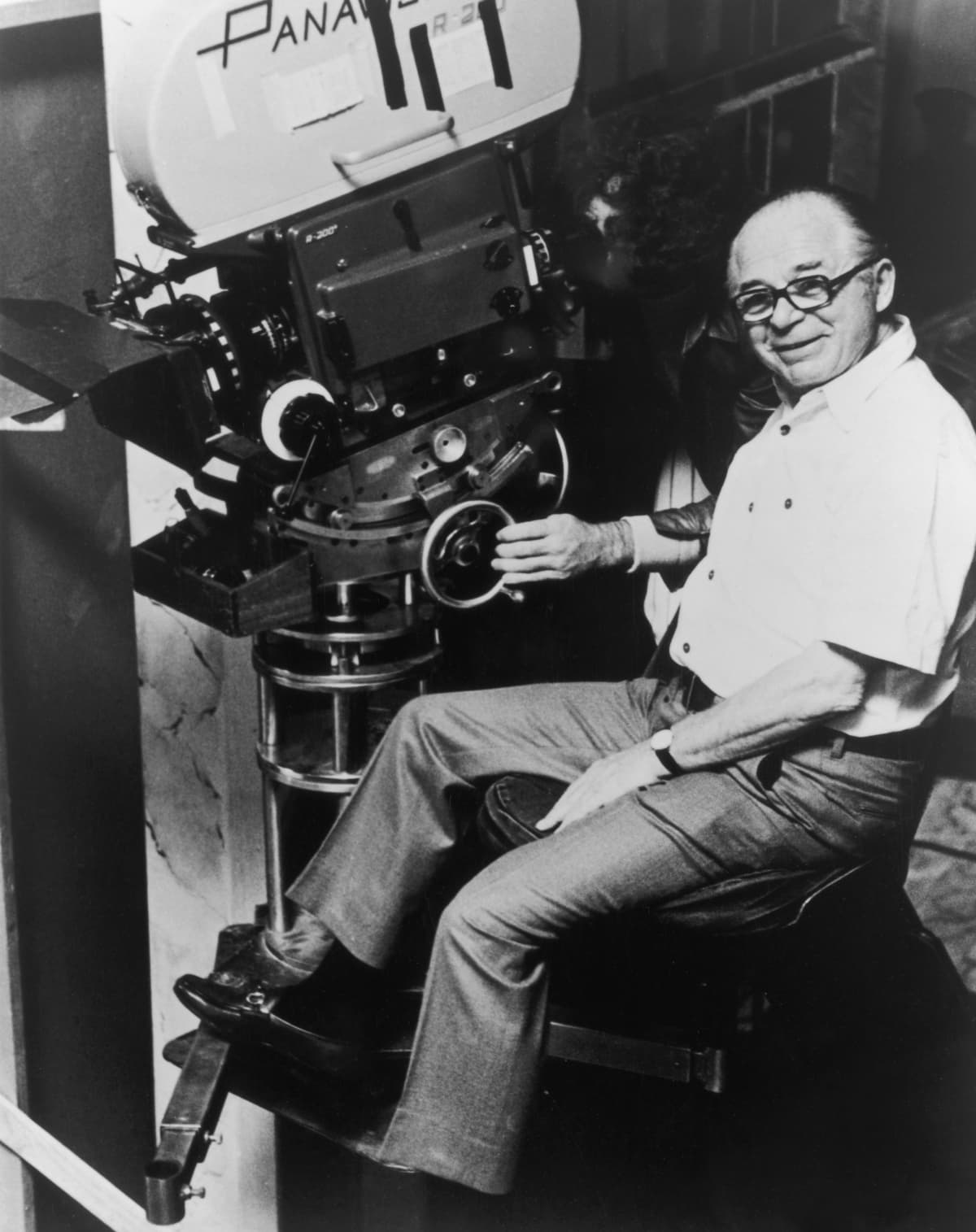 circa 1965:  Austrian-Hungarian-born director Billy Wilder (1906 - 2002) smiles while sitting in front of a cameraman on one of his film sets. The cameraman looks through the viewfinder on a Panavision motion picture camera.  (Photo by Hulton Archive/Getty Images)