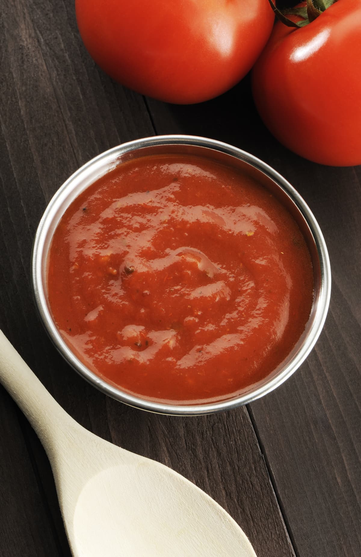 Bowl full of spicy tomato or marinara sauce with wooden spoon and tomatoes in background. More tomatoes in lightbox below...
