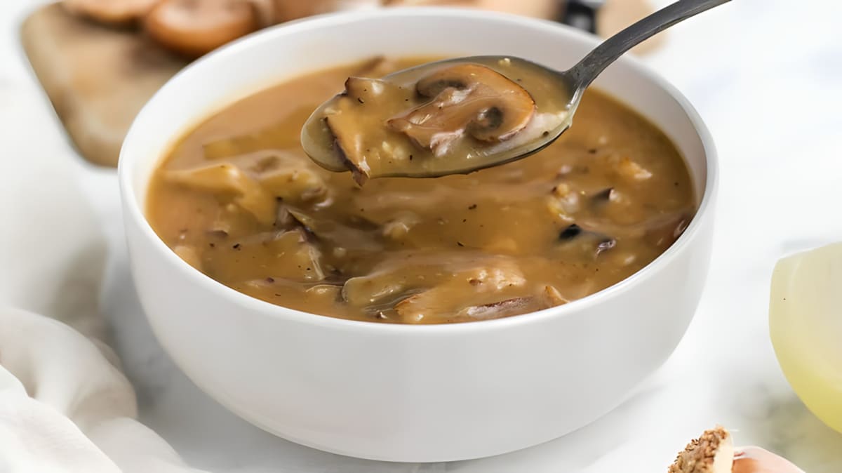 Spoon holding mushroom gravy over a bowl