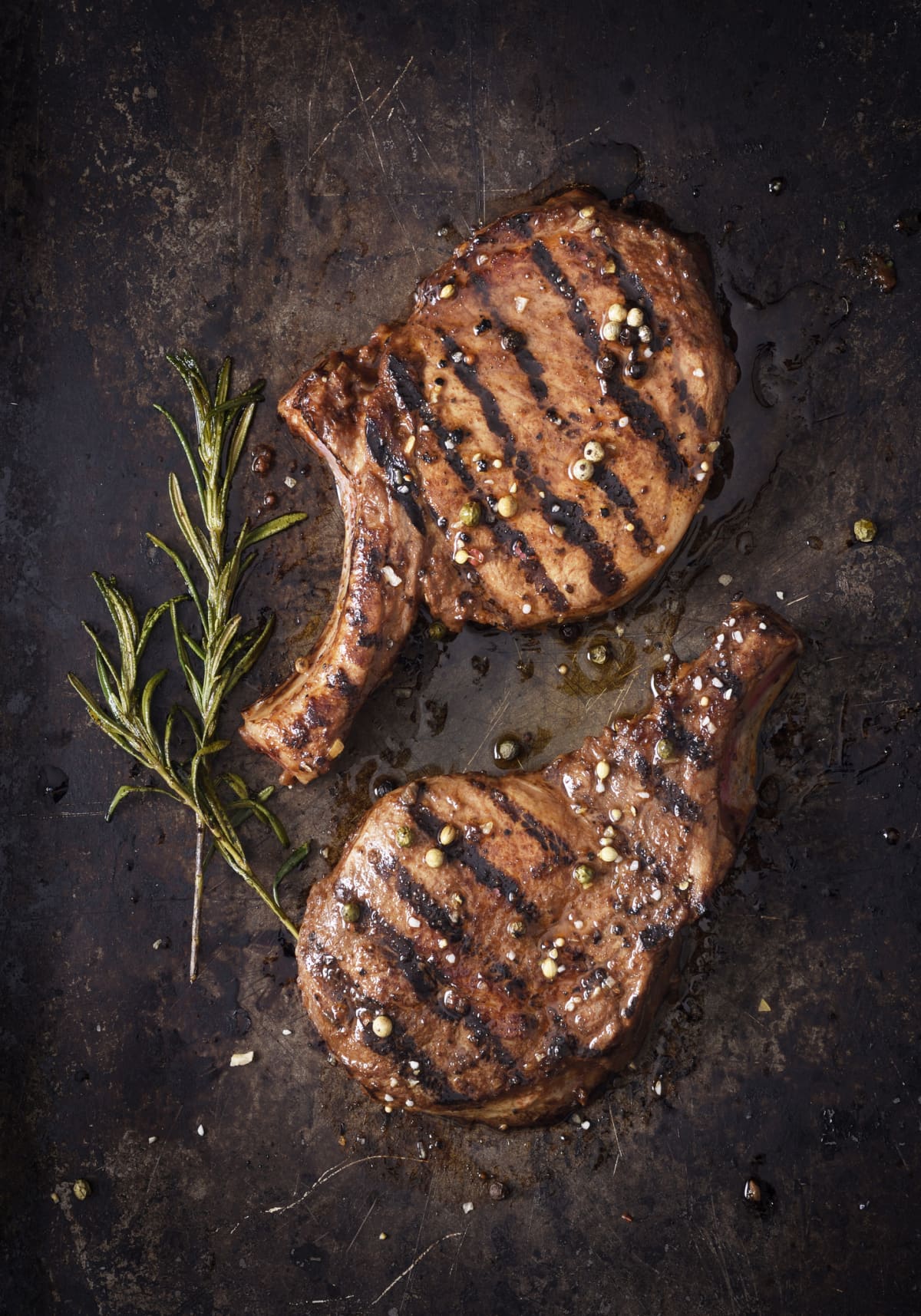 Two juicy grilled steaks with herbs and peppers on a dark background