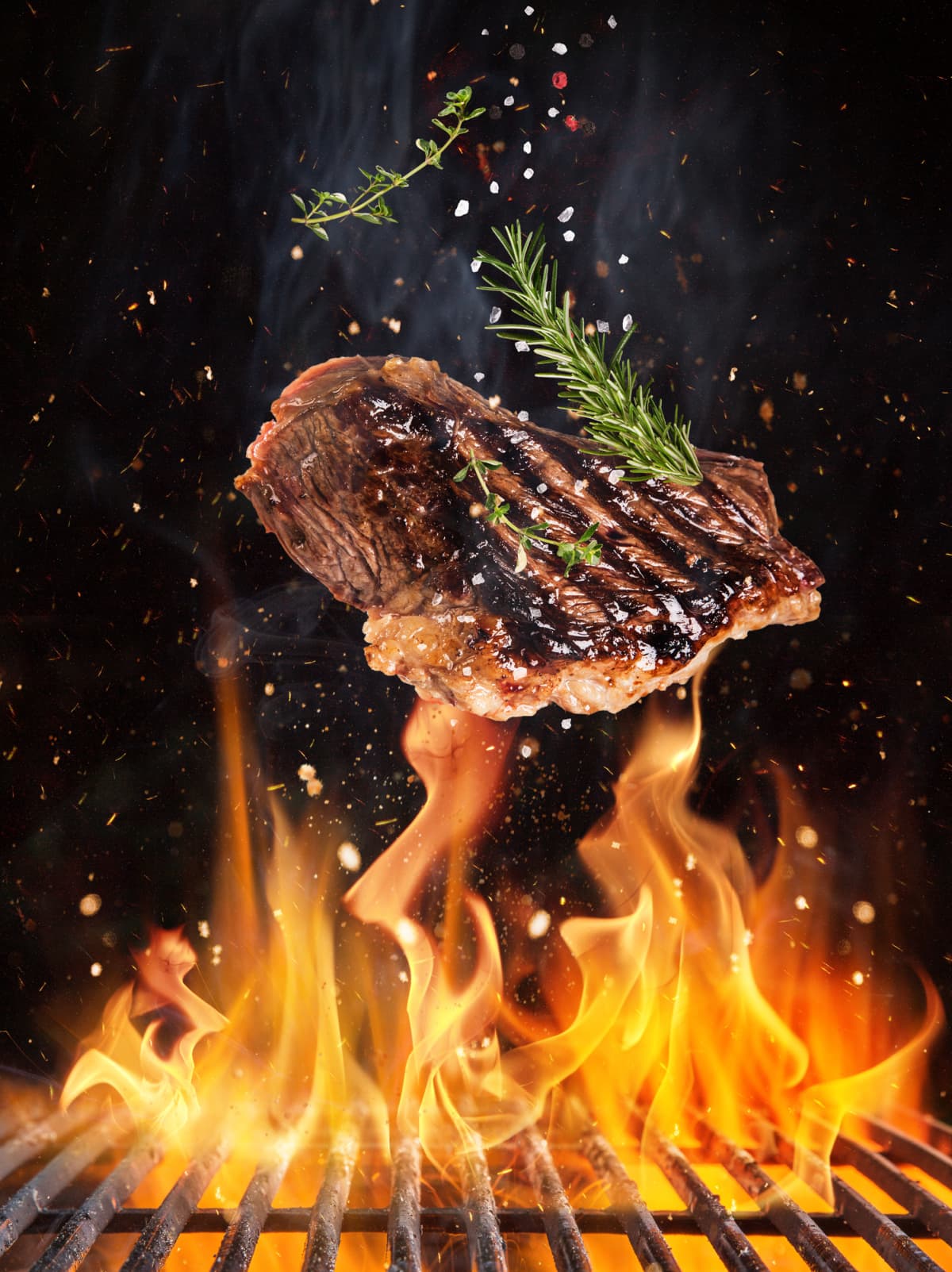 Tasty beef steaks flying above cast iron grate with fire flames. Freeze motion barbecue concept.
