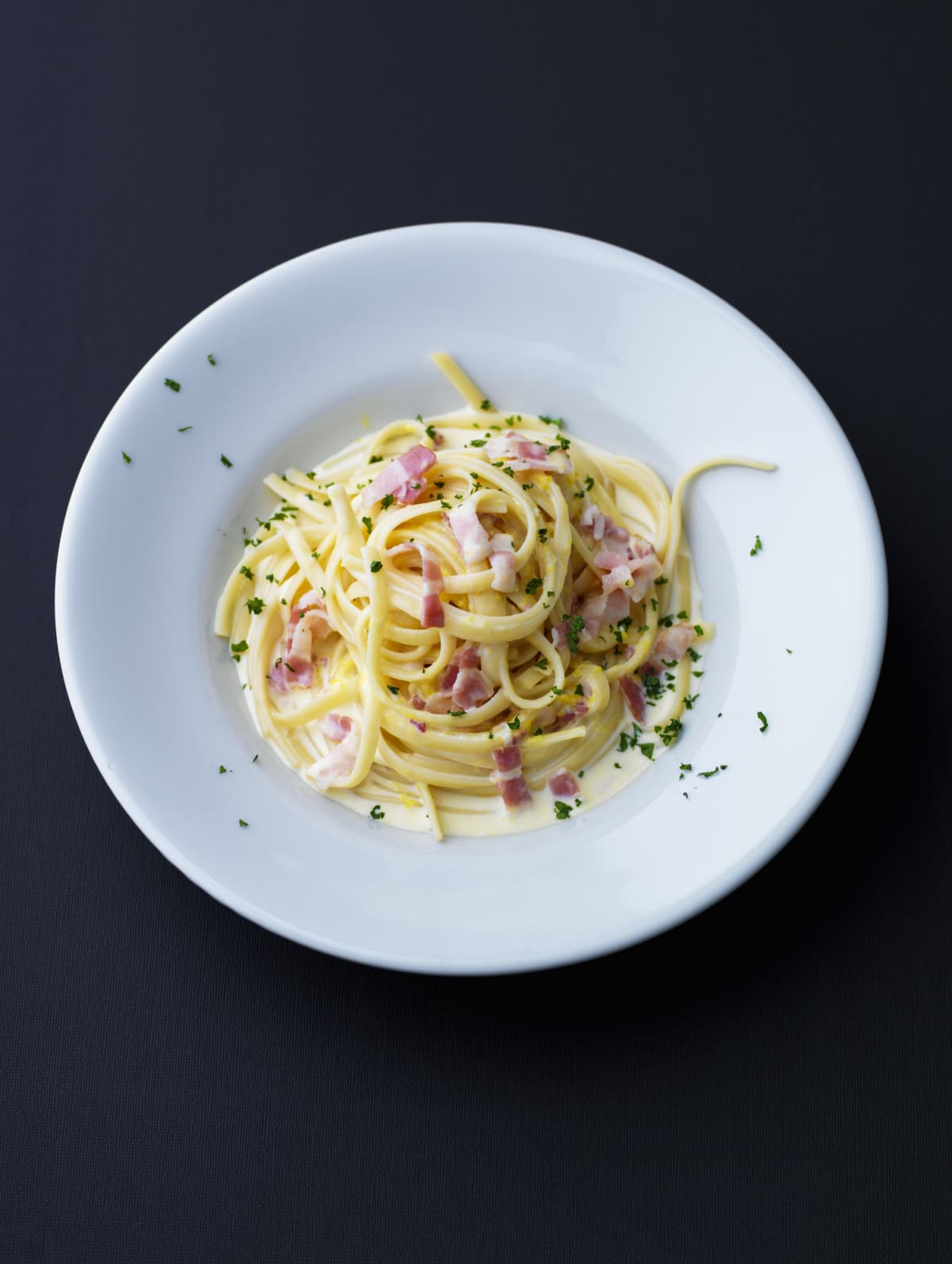 Plate of spaghetti carbonara on solid black background
