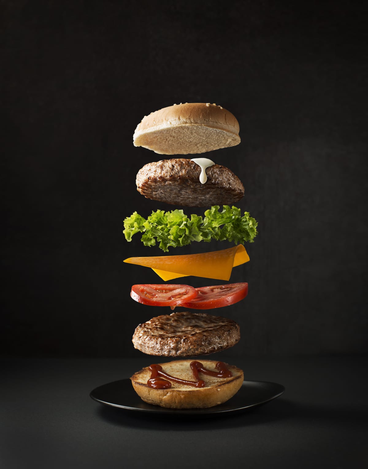 Maxi hamburger with flying ingredients placed on black background. Conceptual jumping Burger. Delicious and attractive hamburger with refreshing ingredients