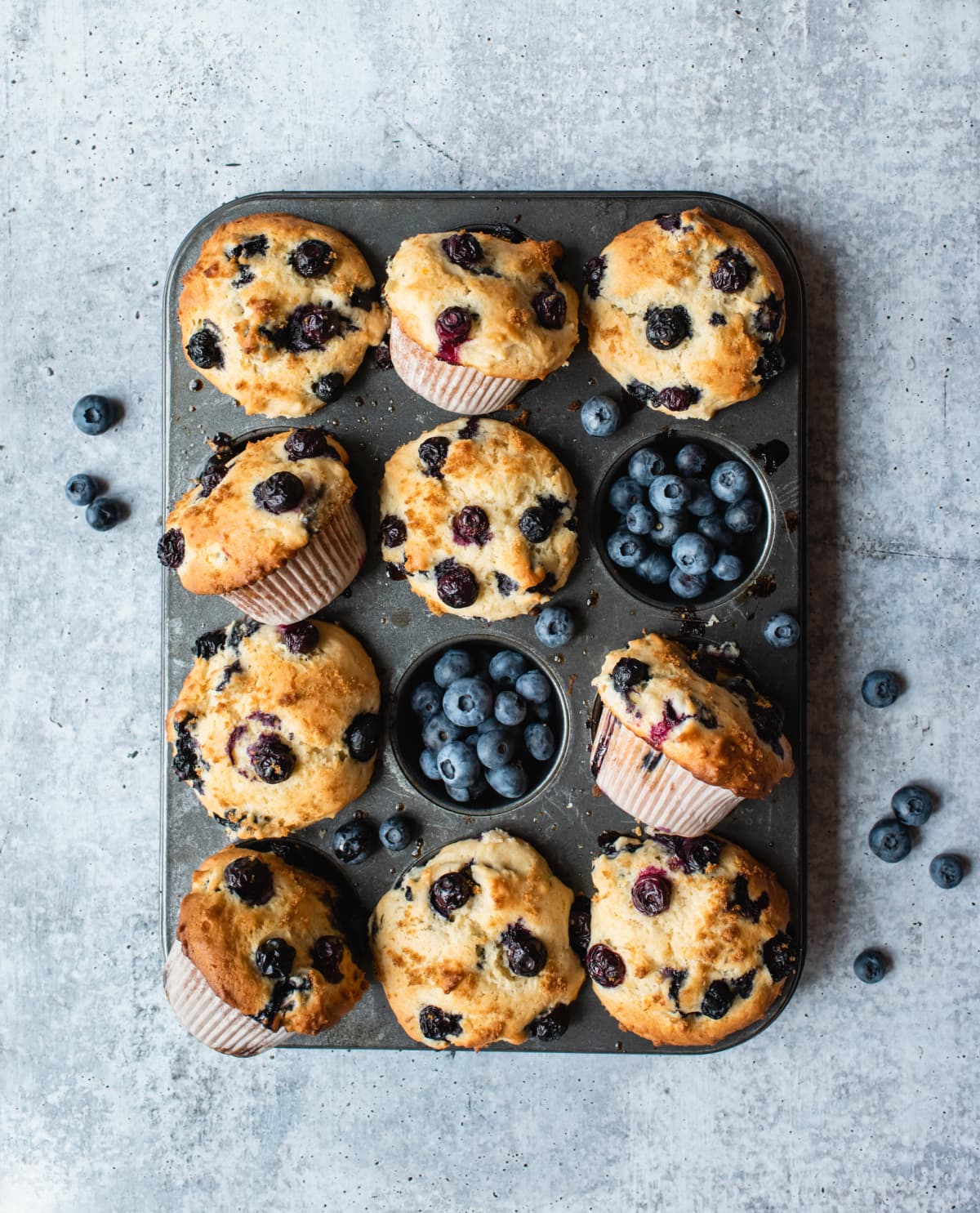 Muffins in a muffin pan with blueberries and some are tilted in odd directions