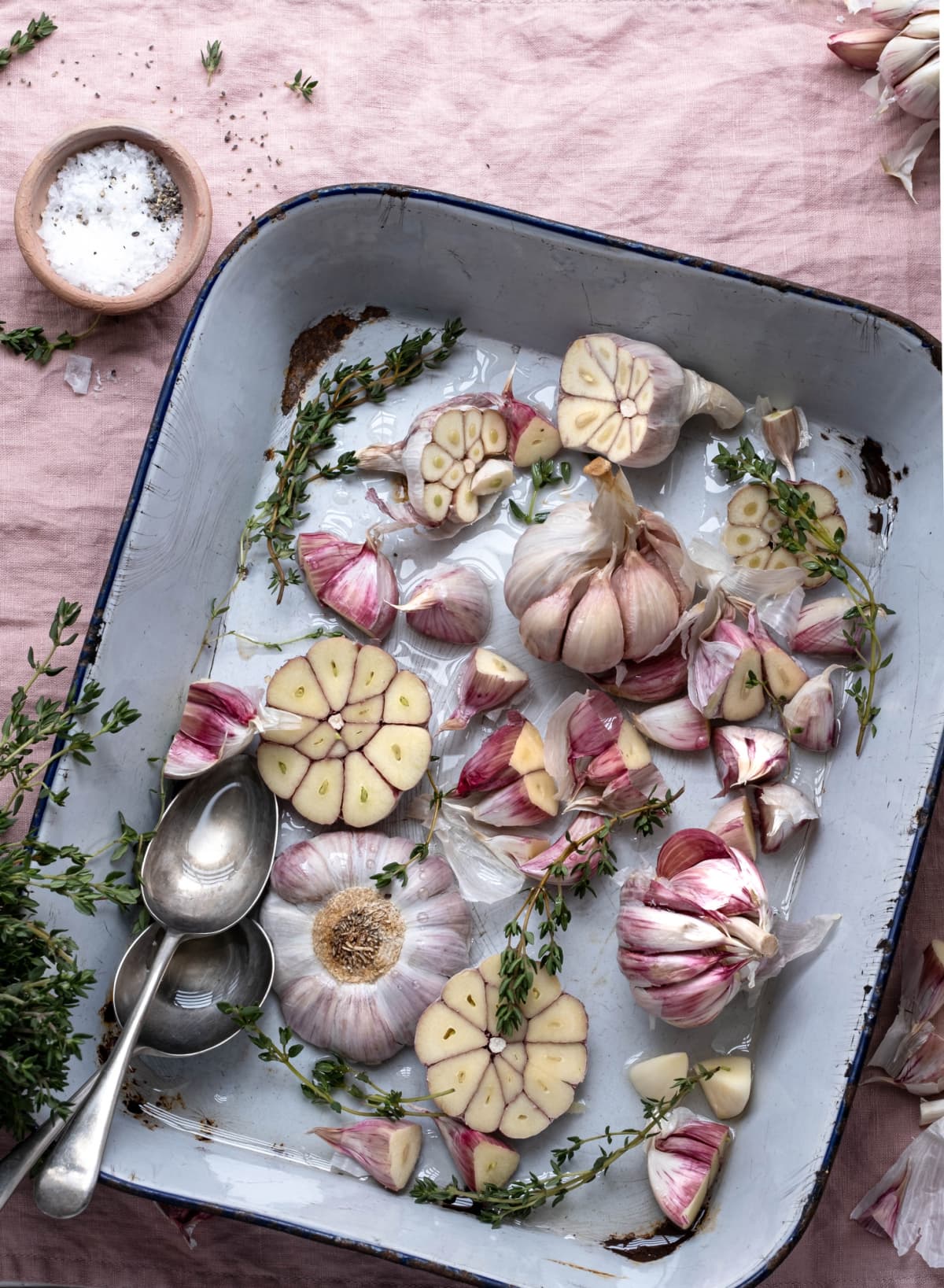 Pink garlic with herbs drizzled with olive oil in a roasting tin.