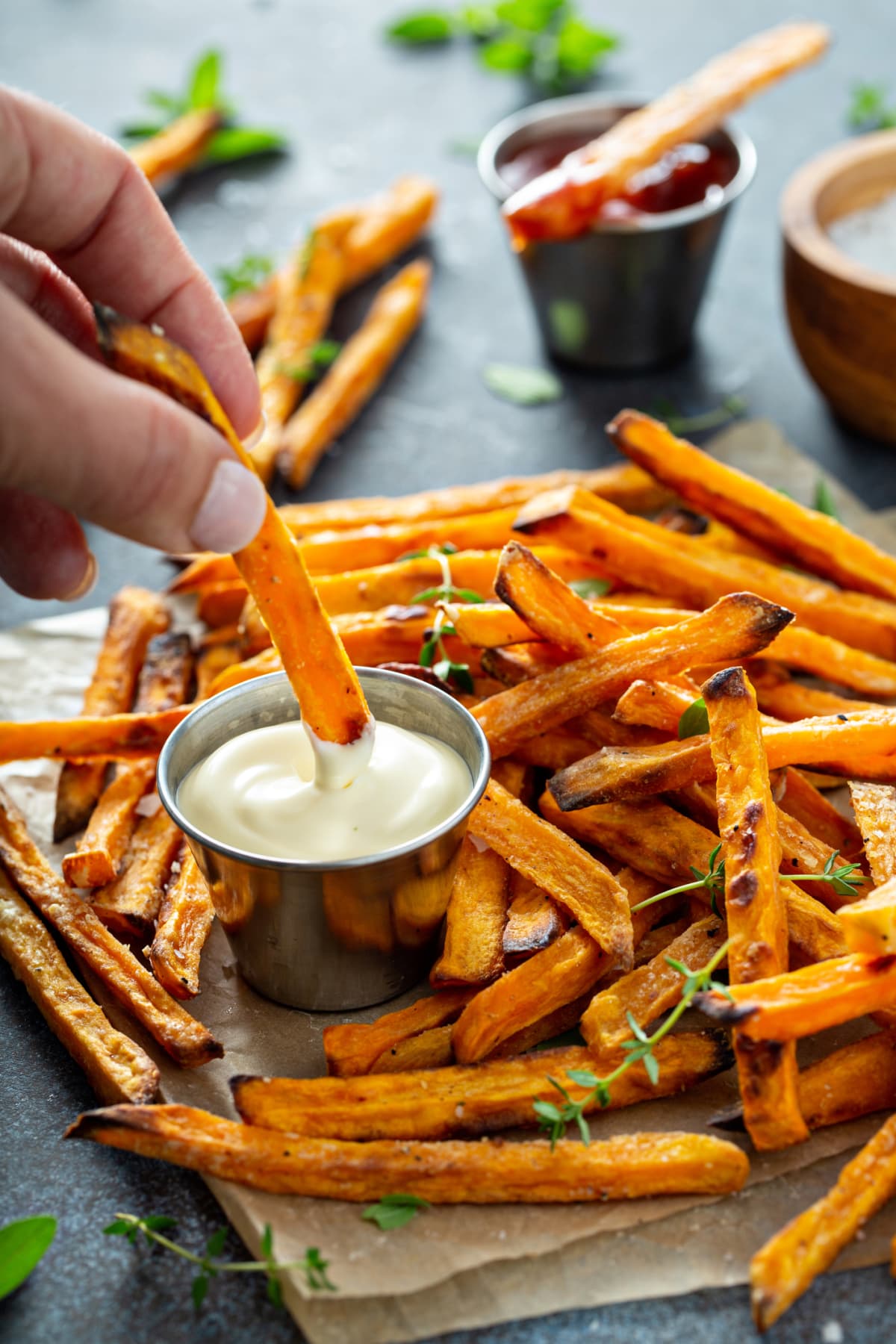 Sweet potato fries with mayo and ketchup and one held in hand being dipped