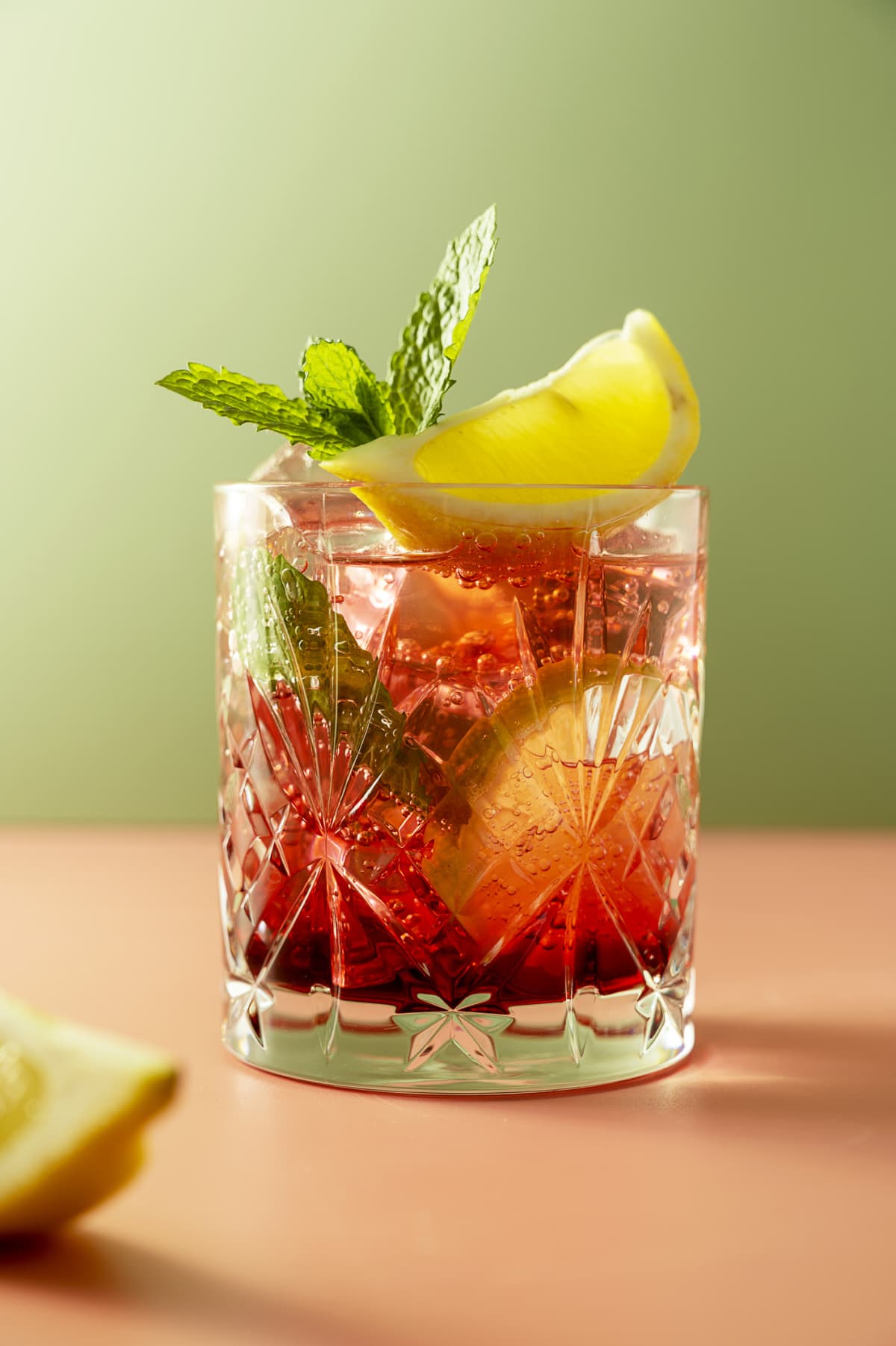 Iced fruit tea or cold berry drink in glass with fresh mint leaves. Refreshing summer drink. Colorful pink and green background