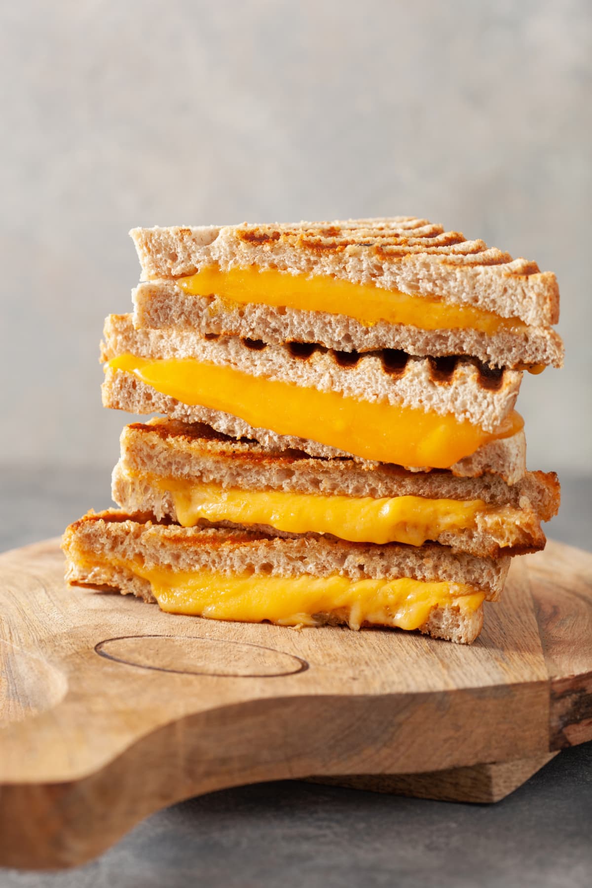 Halved grilled cheese sandwiches stacked on top of a wooden platter