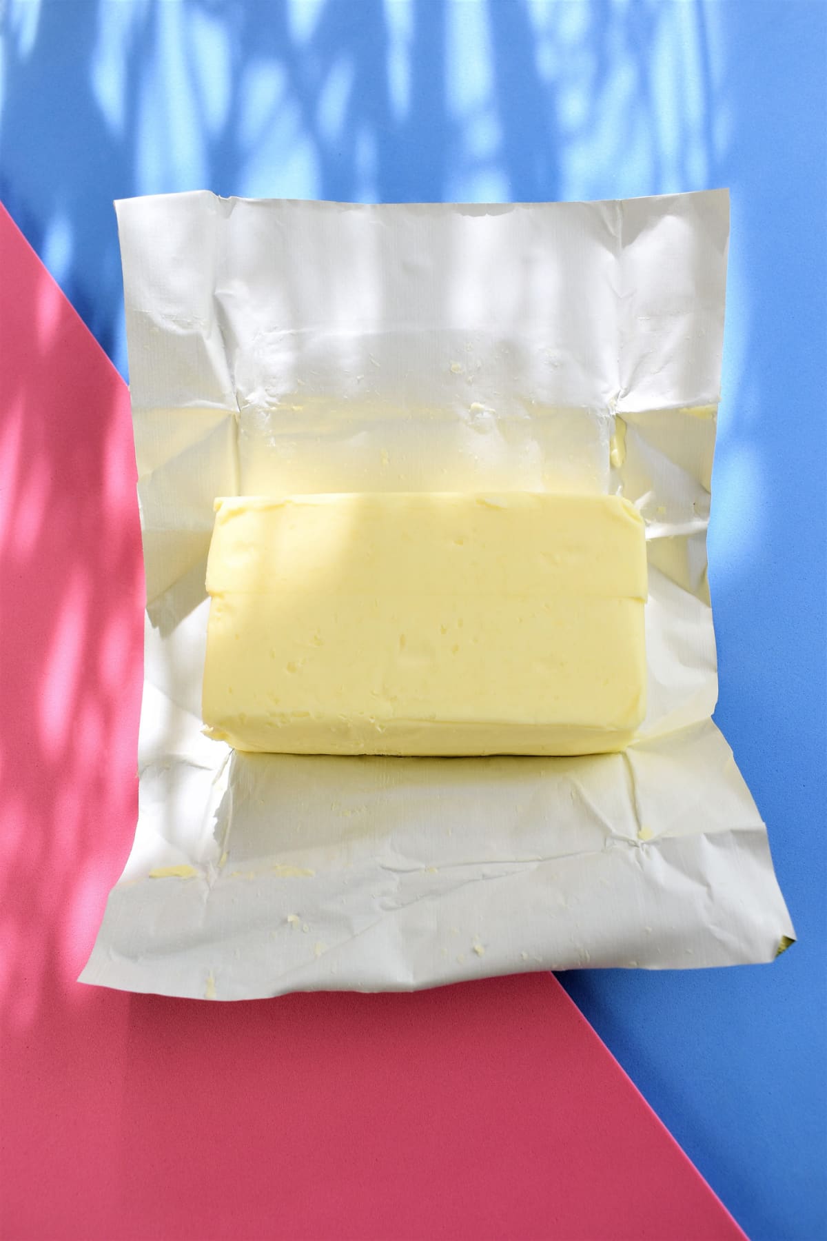 A Block of butter on blue and pink background, top view