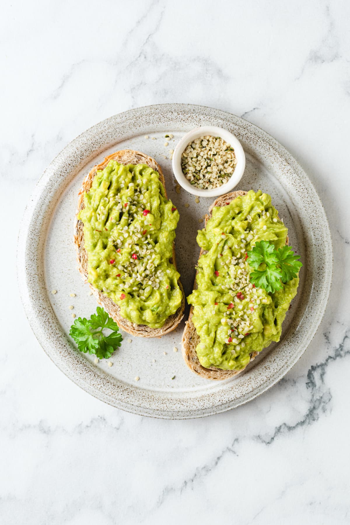 Toast with mashed avocado and hemp seeds on a plate. Healthy vegan snack. Top view, marble background